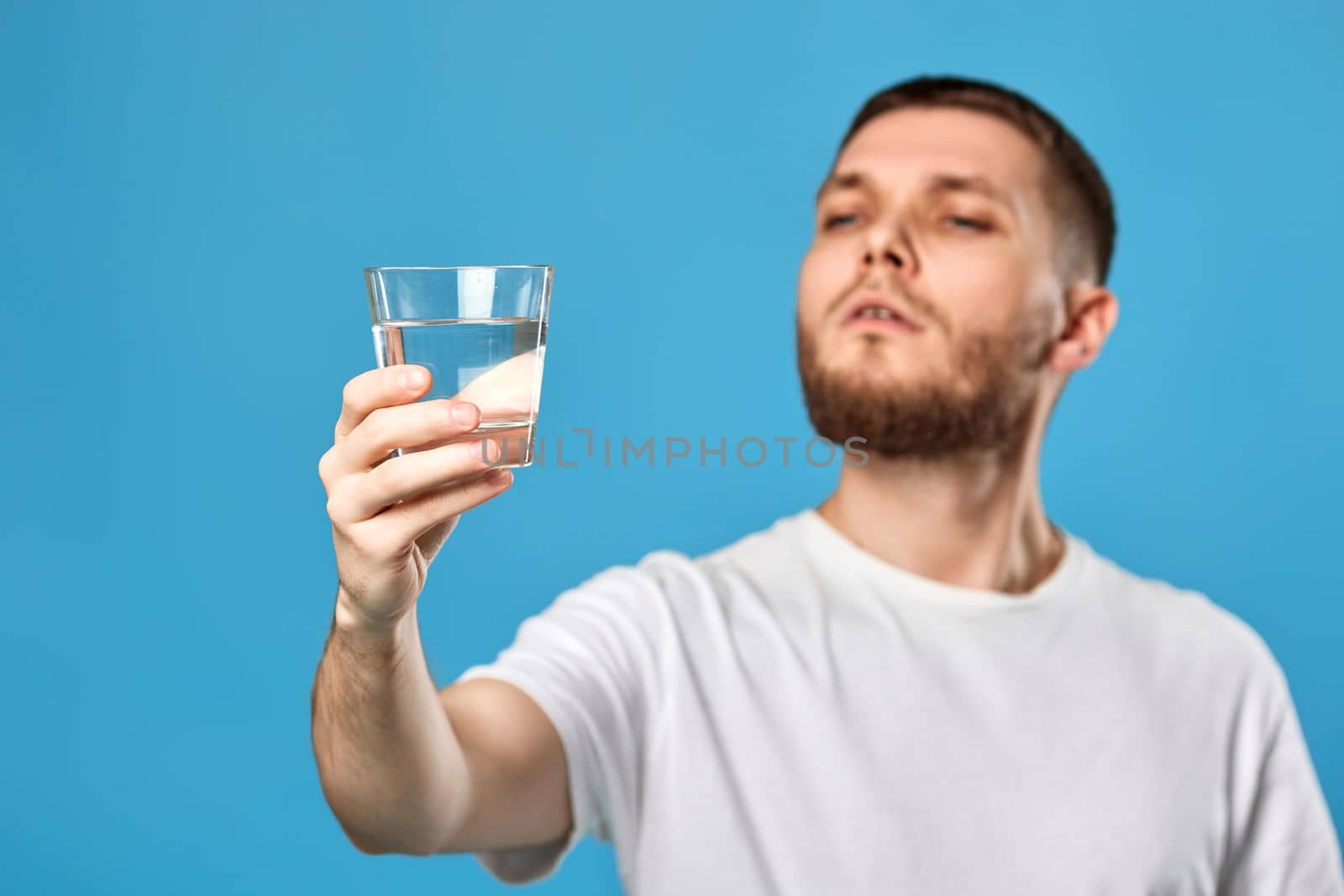 handsome bearded man with drinking glass of water smiling happy on blue background. focus on glass