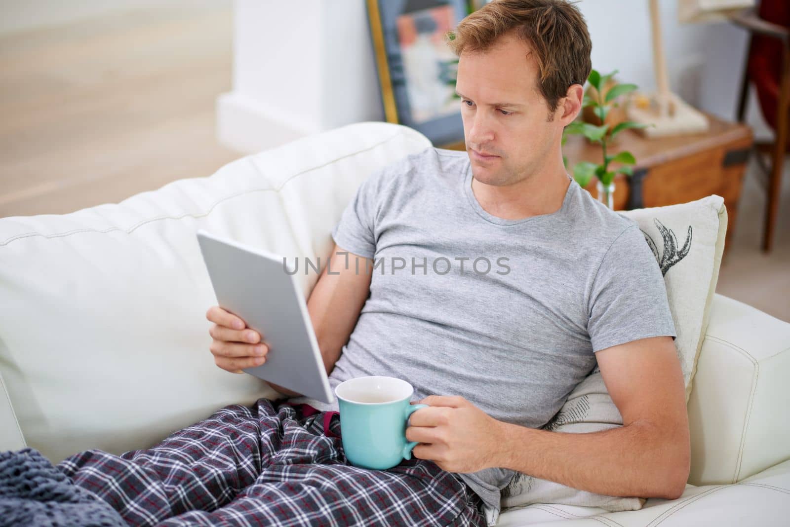 Laid-back day at home. a handsome man drinking coffee while using his tablet at home