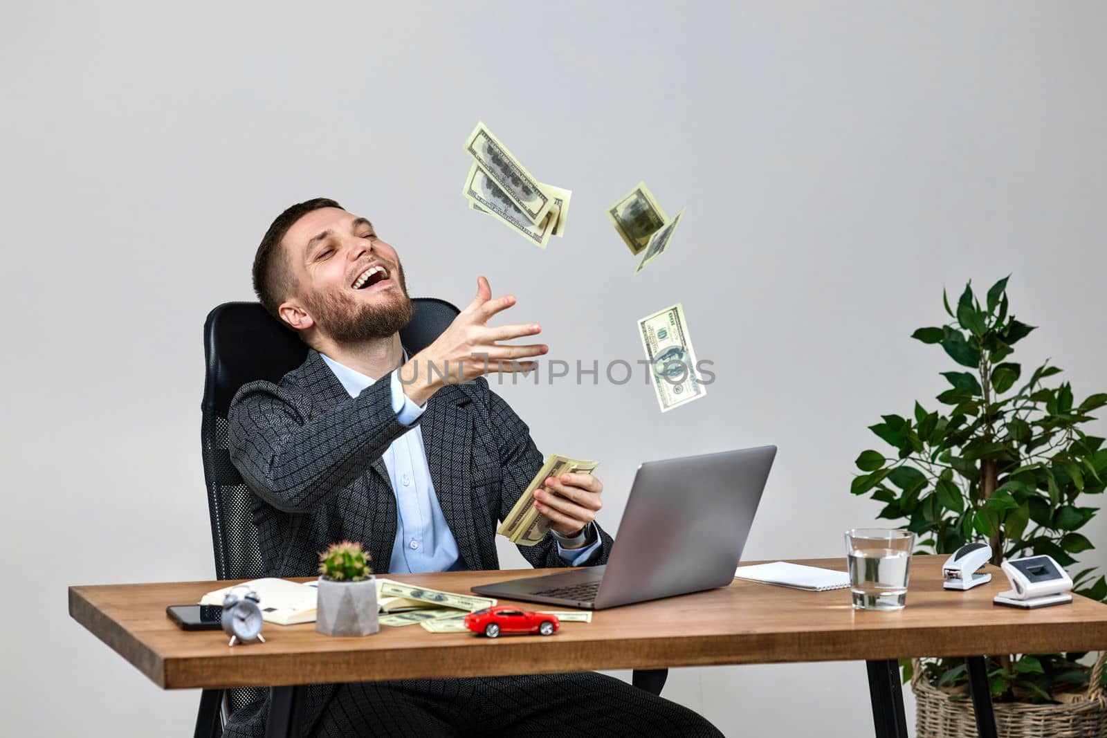 young bearded businessman working on laptop and throwing money by erstudio