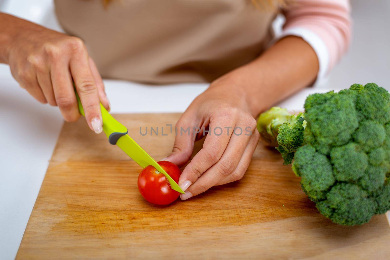 Close-up of a female hands cutting tomato on the kitchen board with broccoli on it.