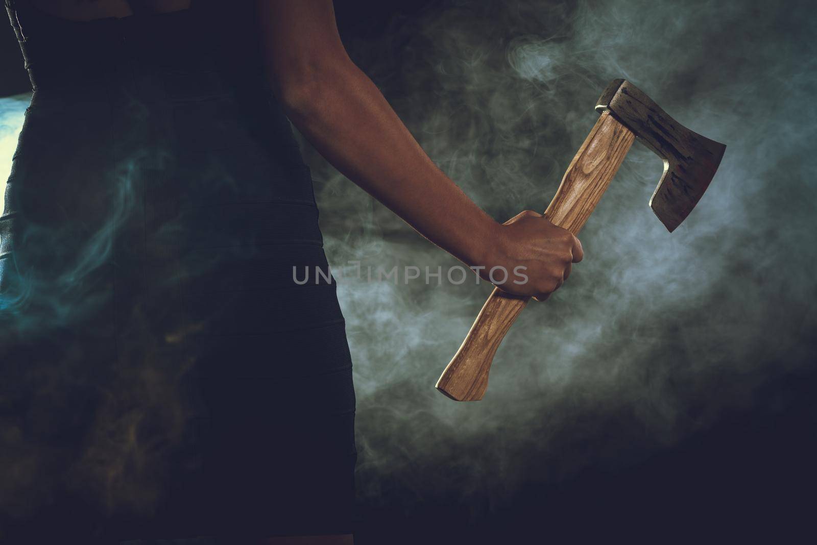 Close-up of a woman's hand with a axe in a smoky dark space. 