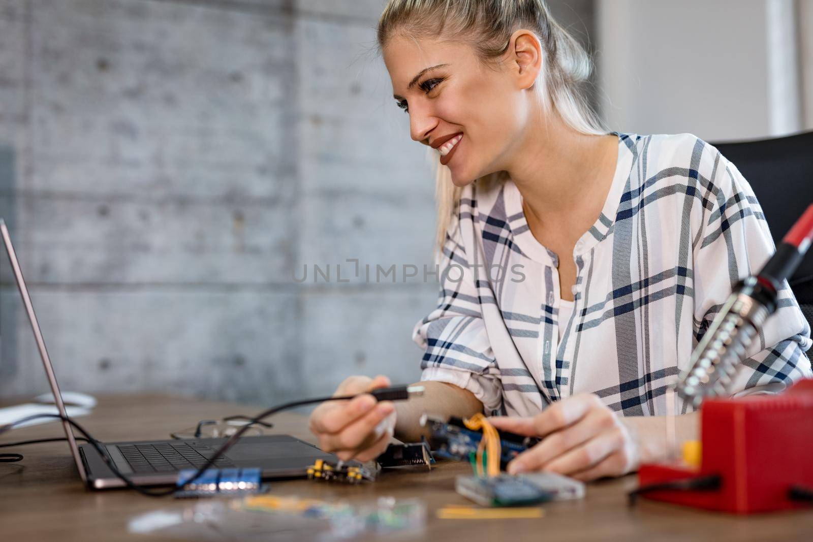 Young smiling woman technician focused on the repair of electronic equipment  and checking something on the laptop.