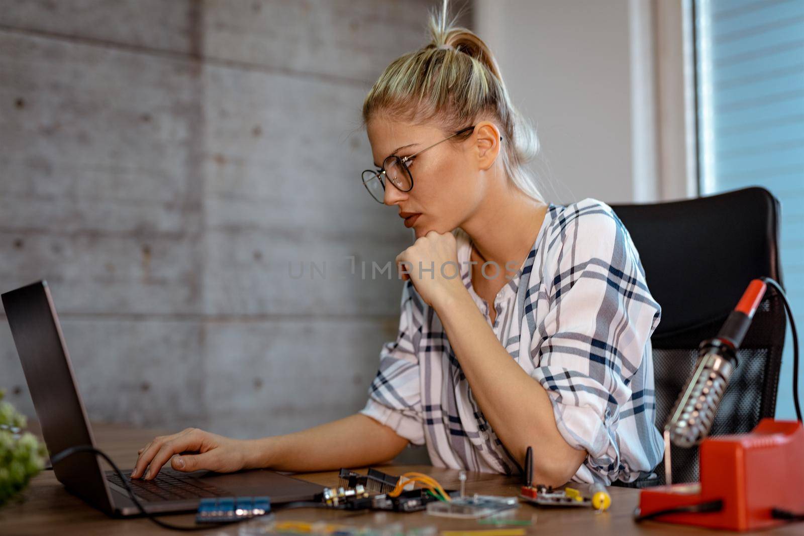 Young woman technician focused on the repair of electronic equipment cecking something on the laptop.