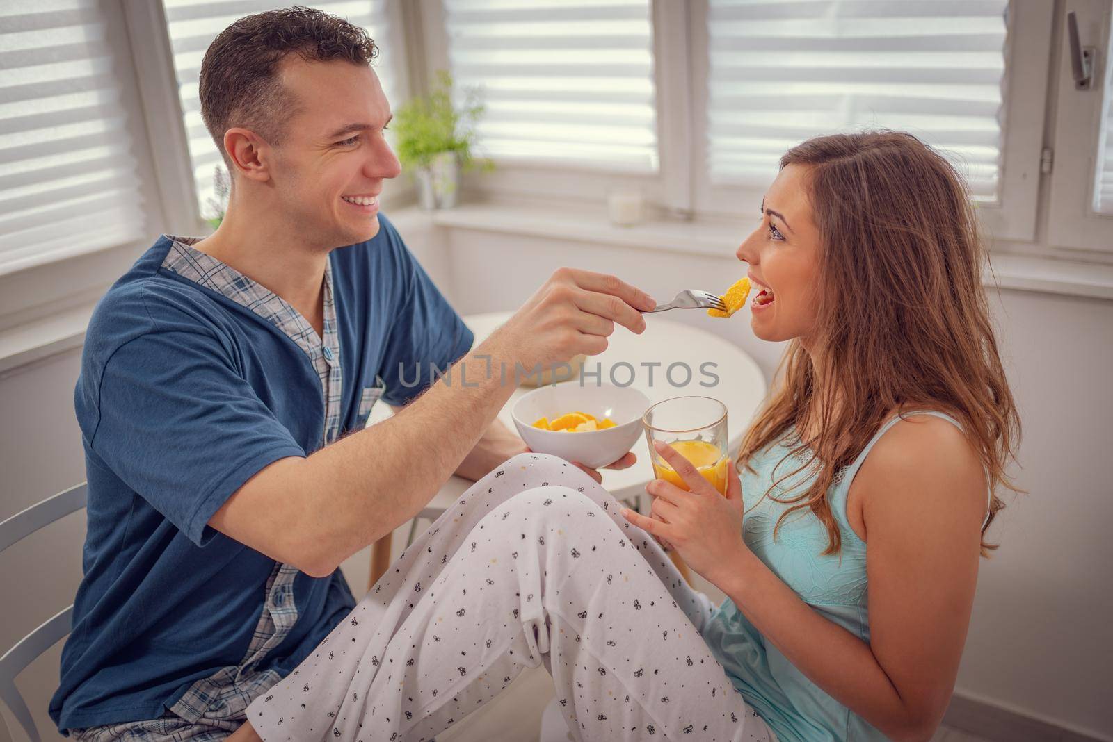 Happy, loving, couple, spending sunday morning in happiness. Man is feeding his loved woman, looking each other with smile. 