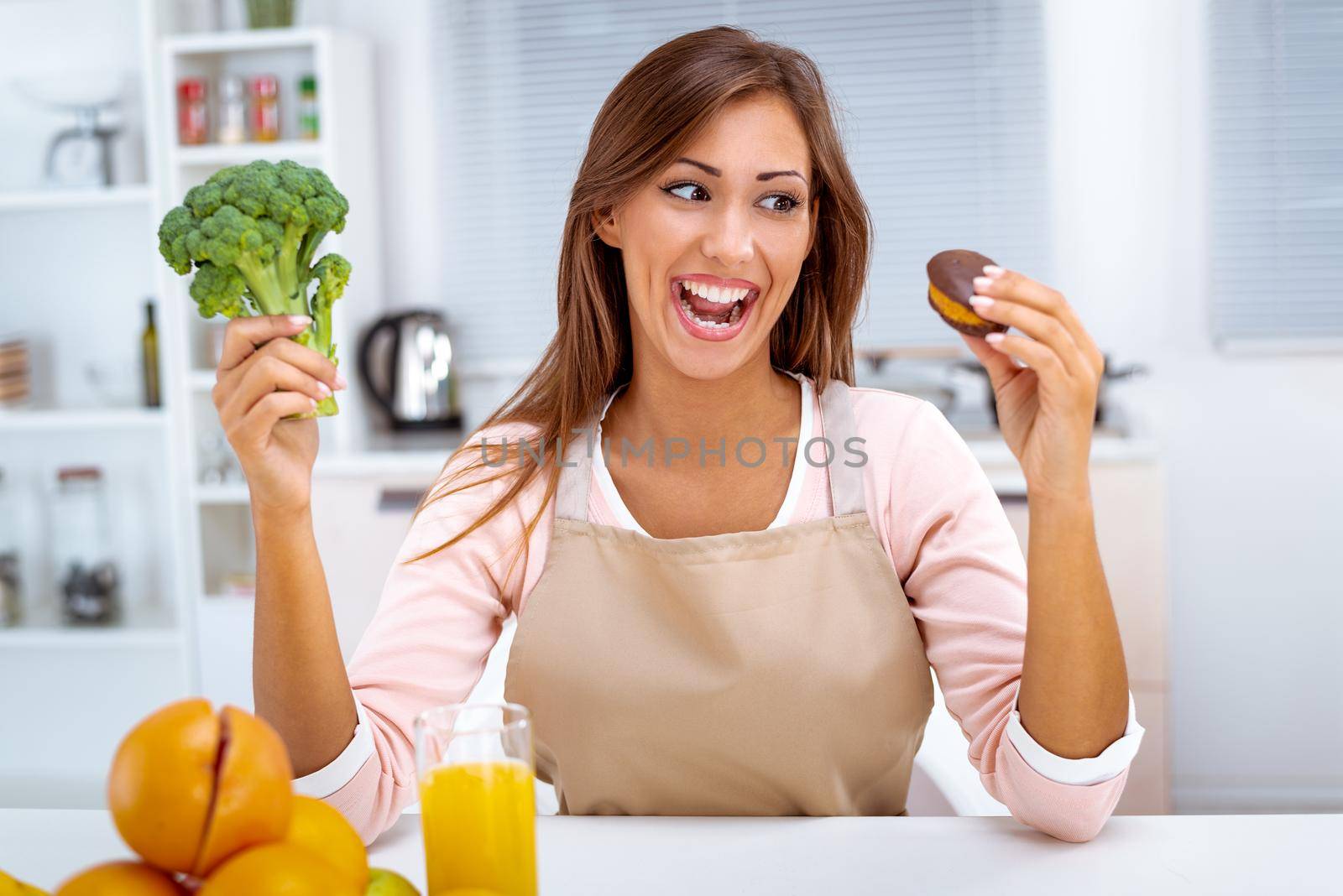 Beautiful young woman in the kitchen decision between broccoli and sweet chocolate cake.
