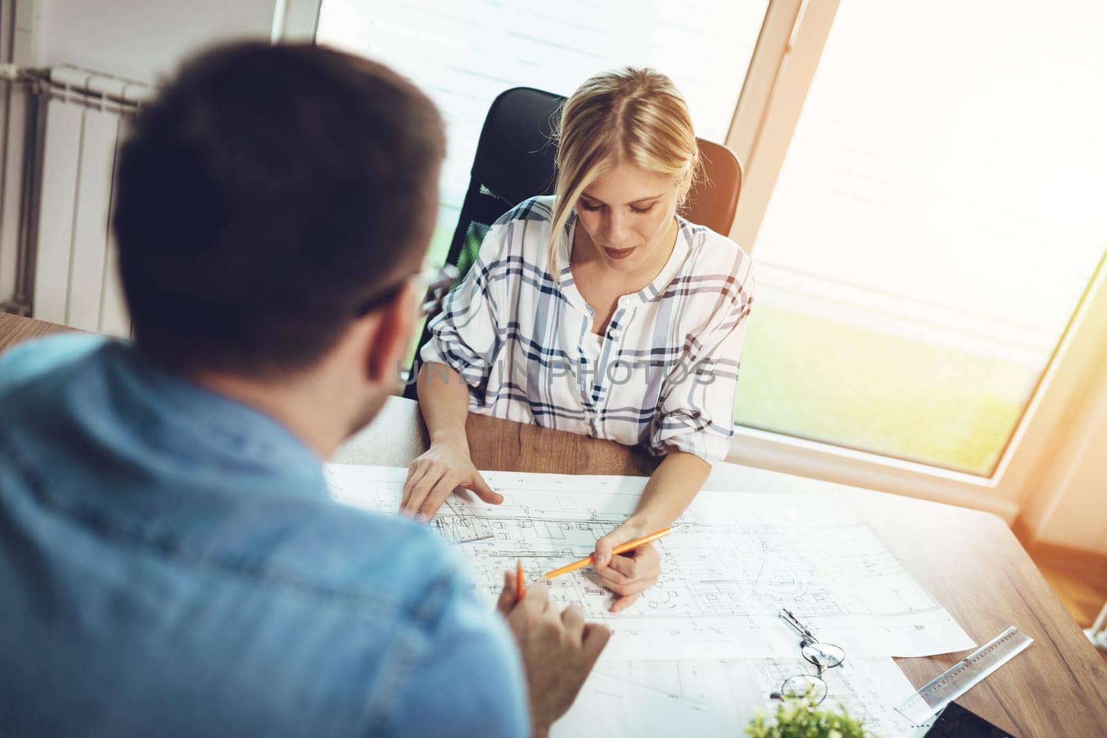 Young pensive architect colleagues talking and analyzing blueprints while working on a new project at the office.
