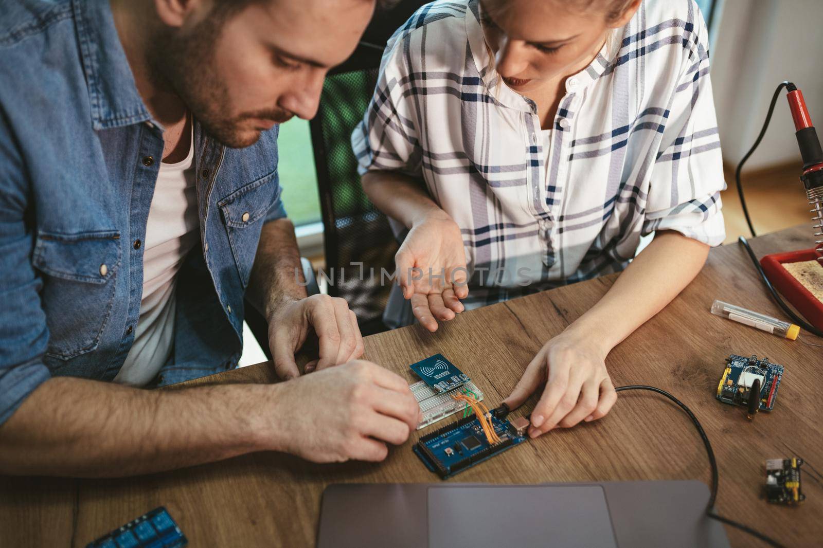 Man is helping woman soldering elements of circuit board.  