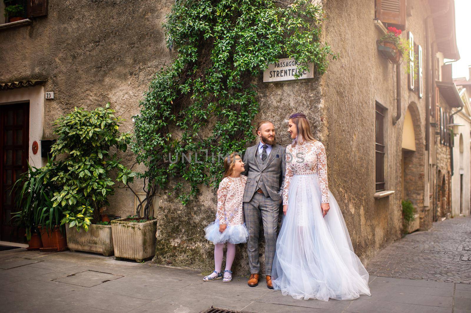 A happy stylish family stands in the old town of Sirmione in Italy by Lobachad