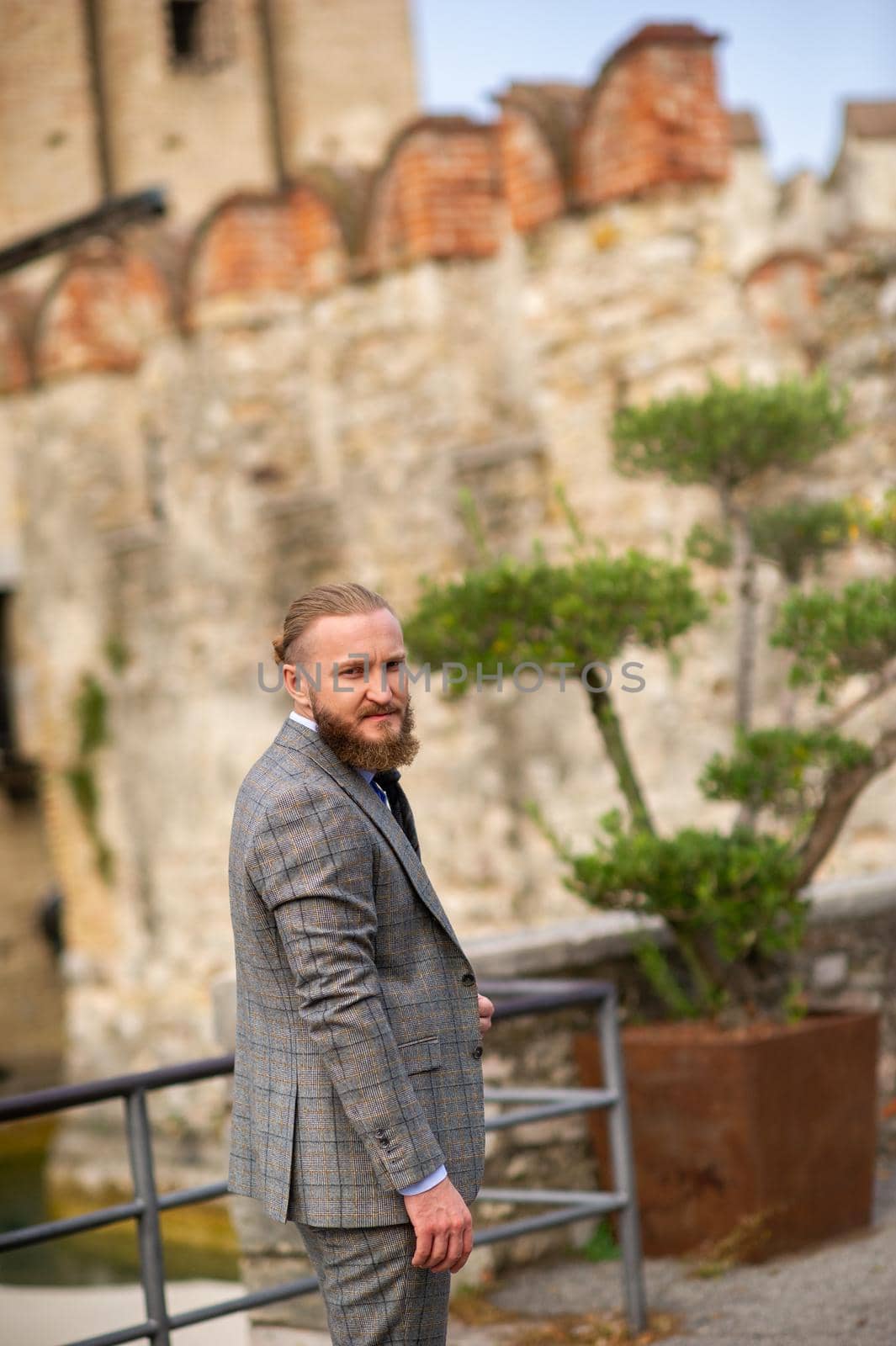 A man with a beard in a strict grey three-piece suit with a tie in the old town of Sirmione, a Stylish man in a grey suit in Italy.