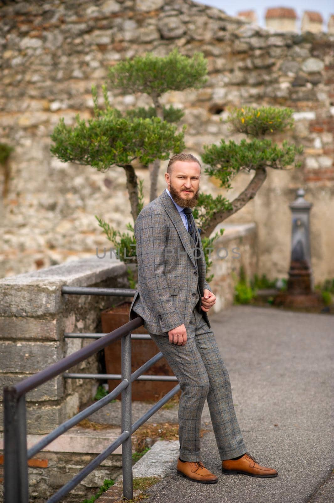 A man with a beard in a strict grey three-piece suit with a tie in the old town of Sirmione, a Stylish man in a grey suit in Italy.