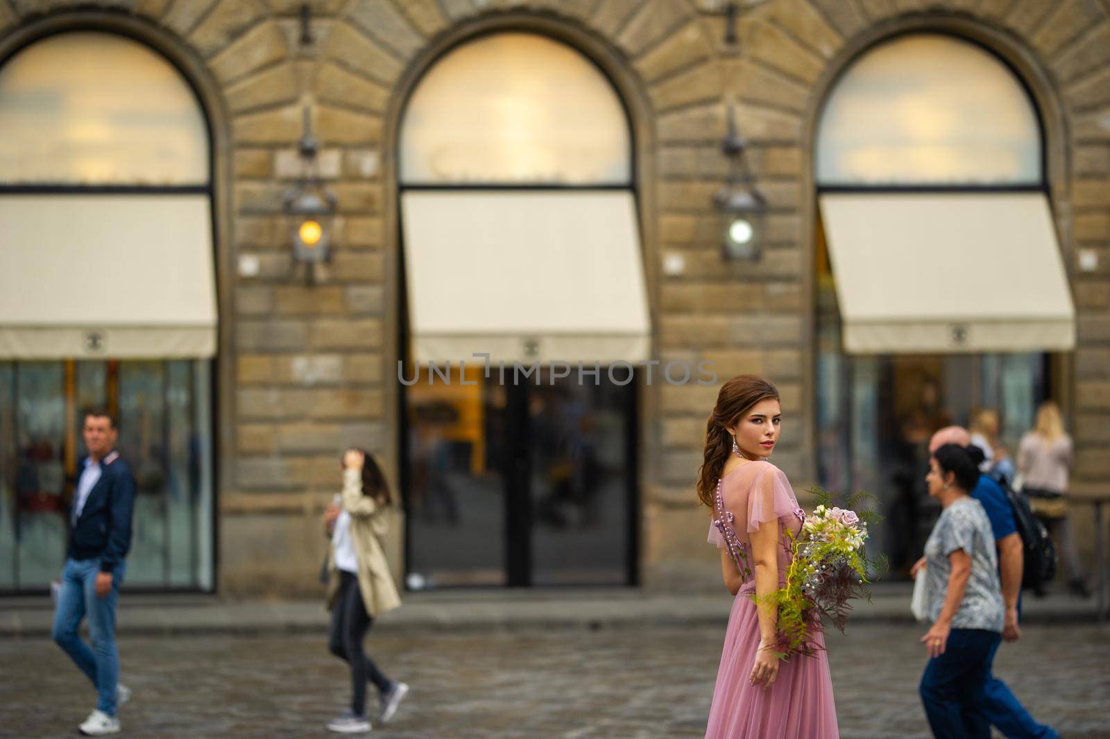 A bride in a pink dress with a bouquet stands in the center of the Old City of Florence in Italy.