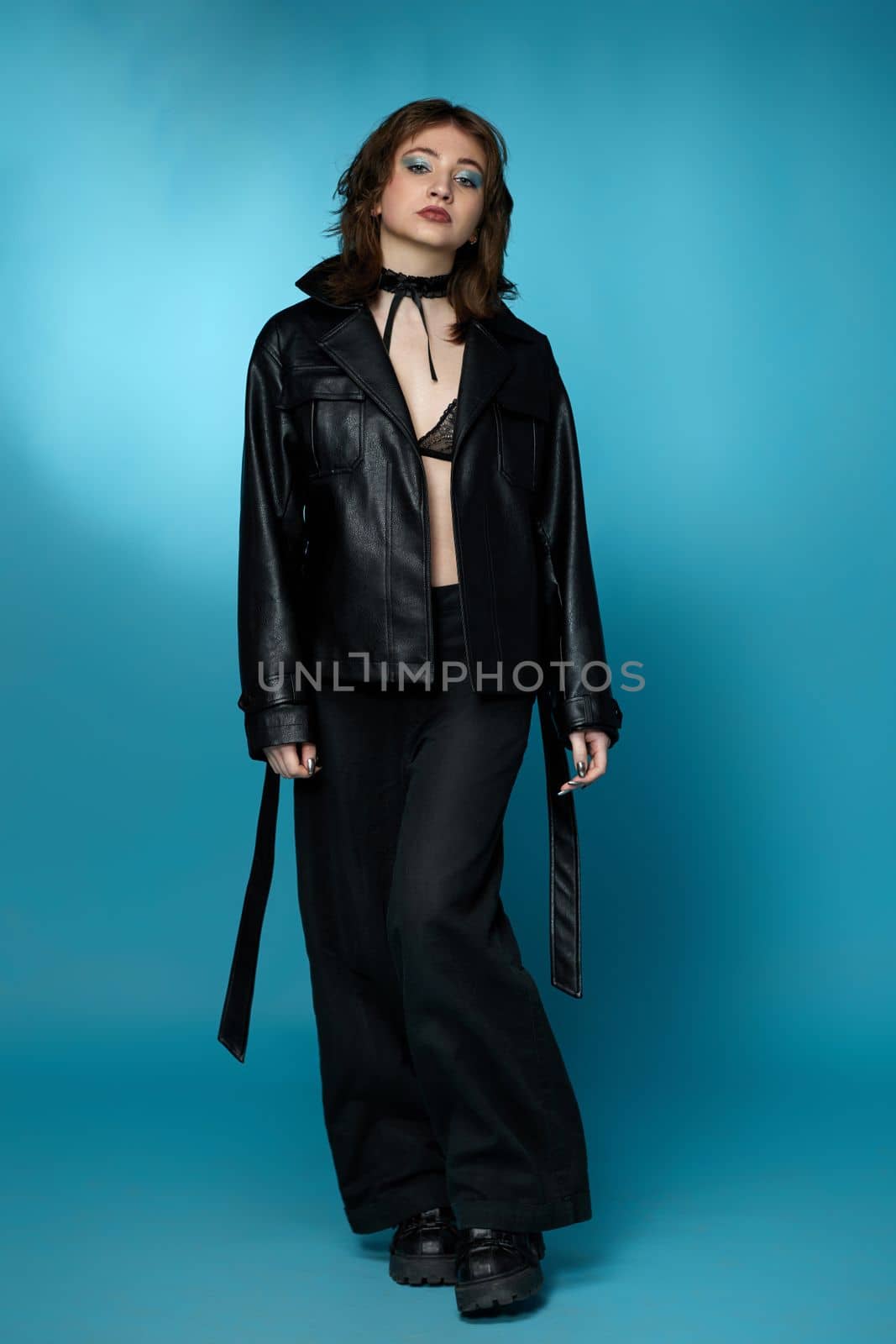 young stylish woman posing in black leather jacket and pants on blue background.
