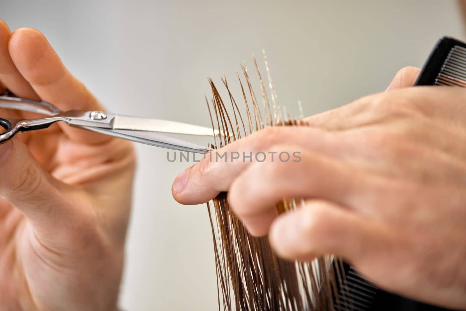 Professional male hairdresser with scissors cutting female hair in salon