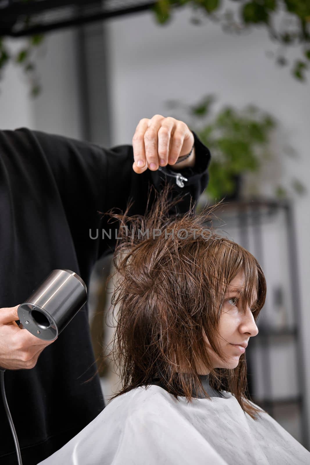 man hairdresser dries female hair with hairdryer after washing by erstudio
