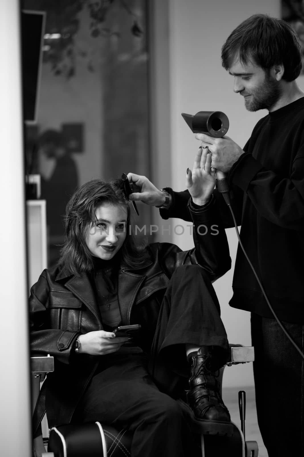 man hairdresser using hair dryer for female hair after washing in the beauty salon.