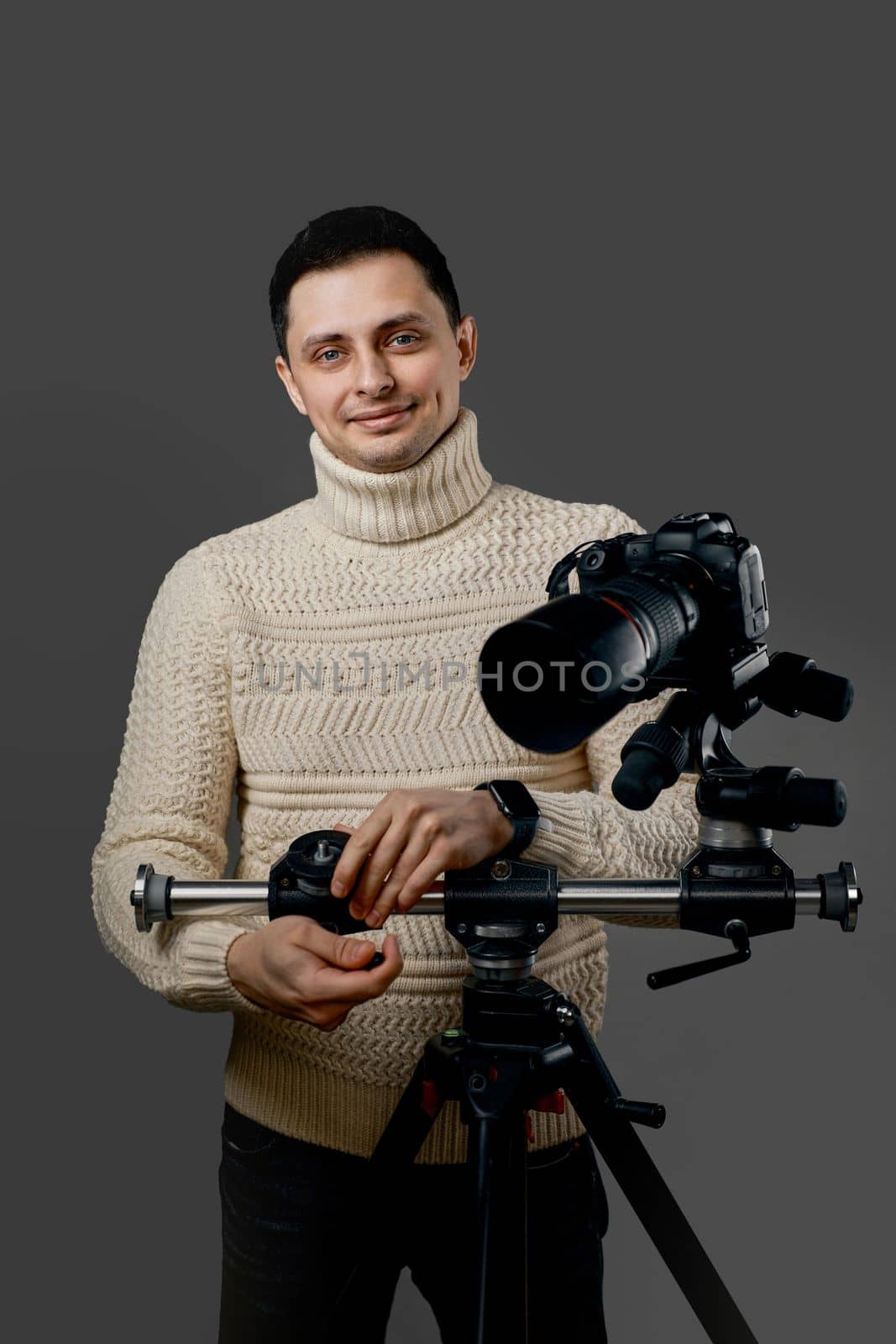 Delighted professional photographer with digital camera on tripod on gray background
