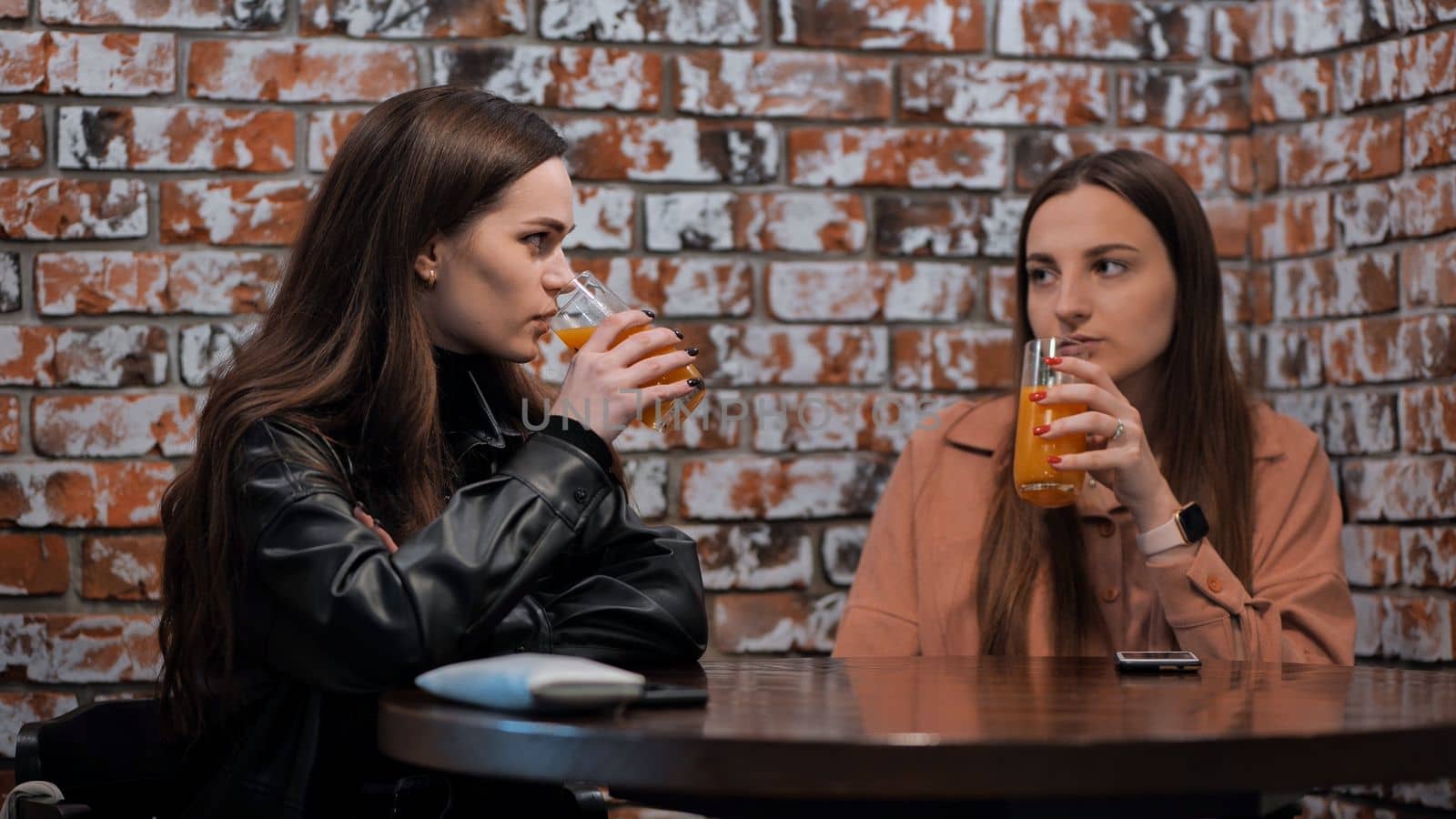 Two brown-haired girls talk in a cafe over glasses of juice