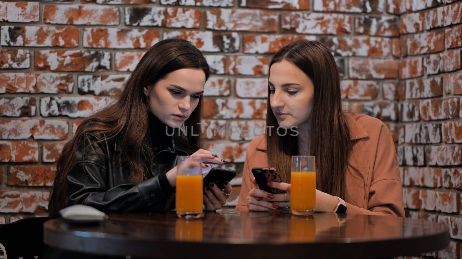 Two beautiful girls are sitting in a cafe and talking with phones. by DovidPro