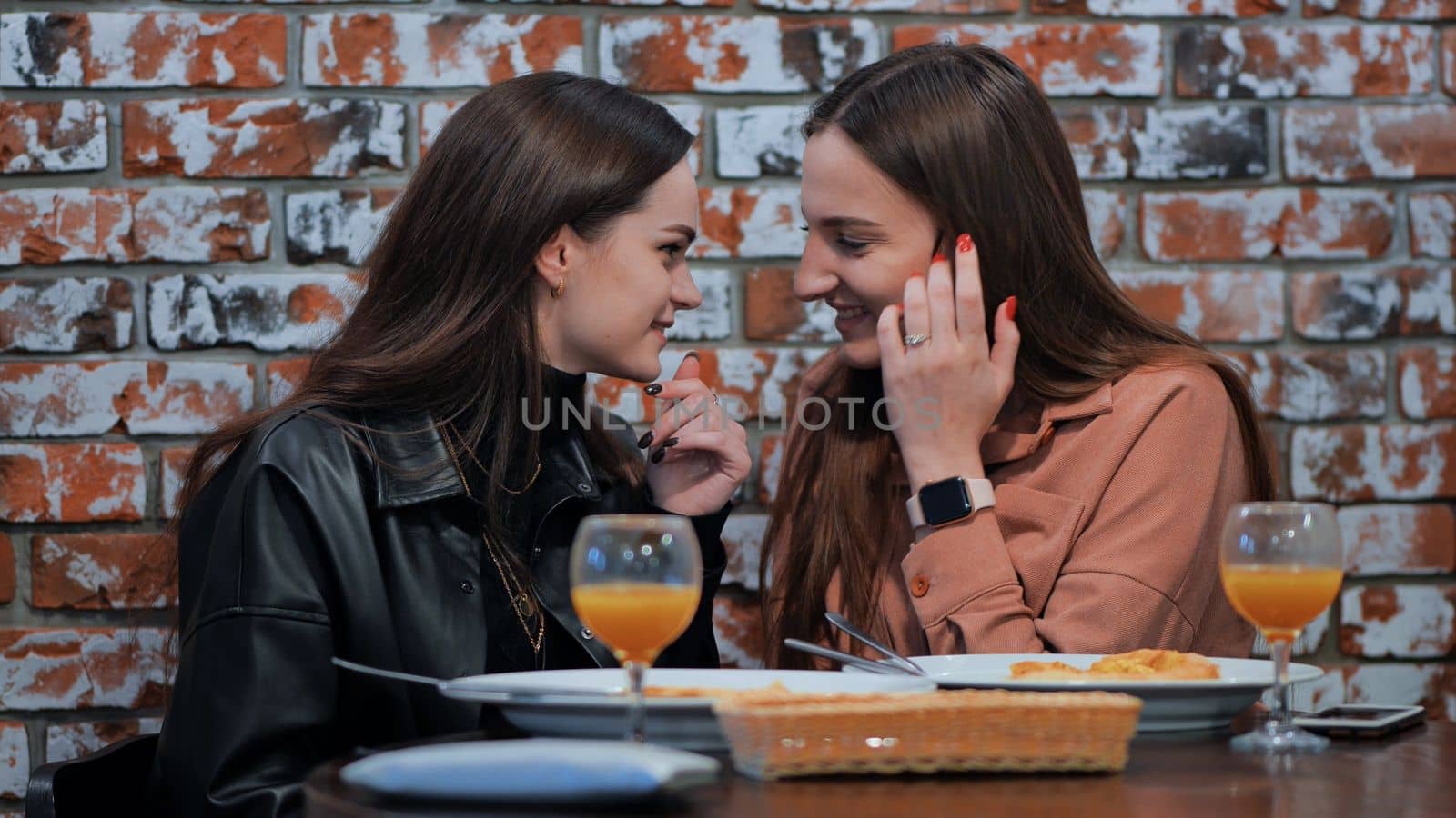 Young and cheerful girls gossip and whisper to each other while sitting in a cafe