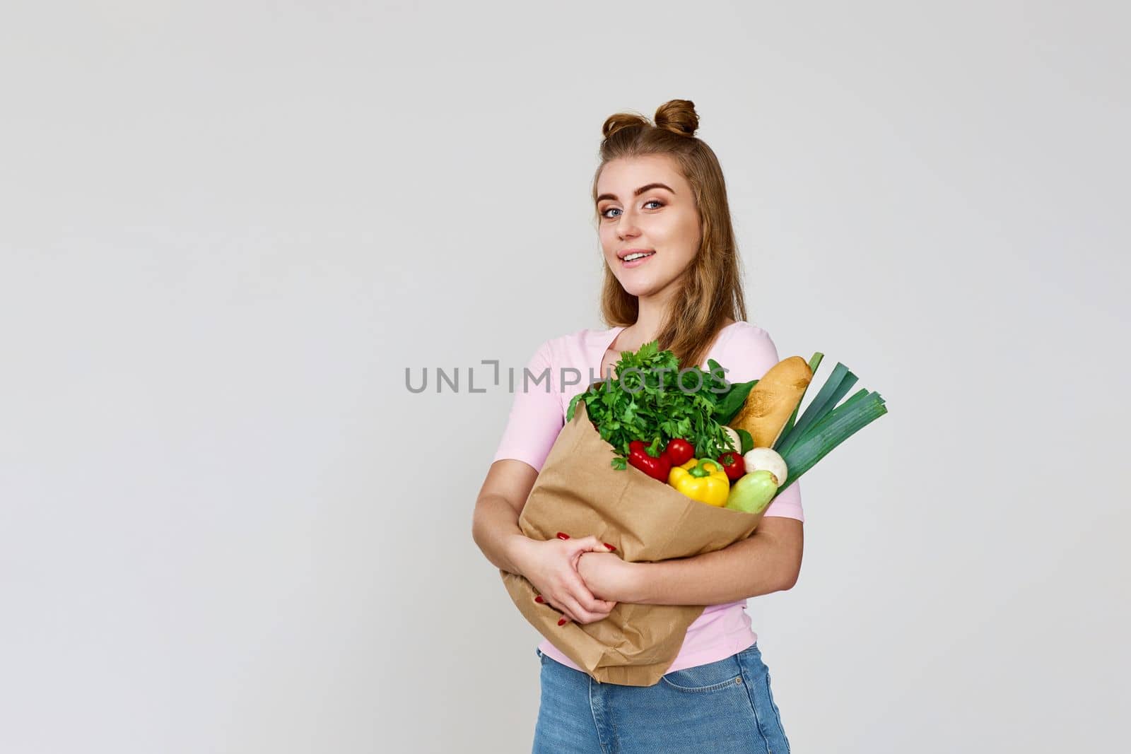 Young smiling caucasian vegetarian woman hold paper bag with vegetables after shopping on gray background