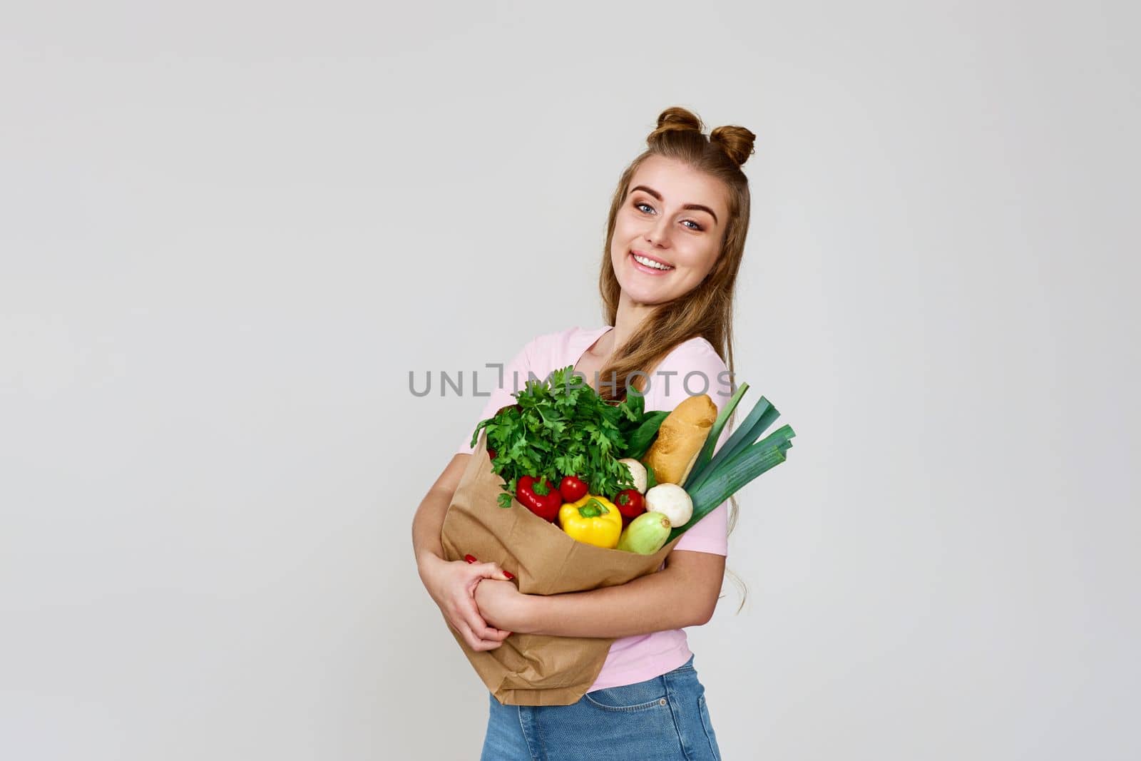 Young smiling caucasian vegetarian woman hold paper bag with vegetables after shopping on gray background