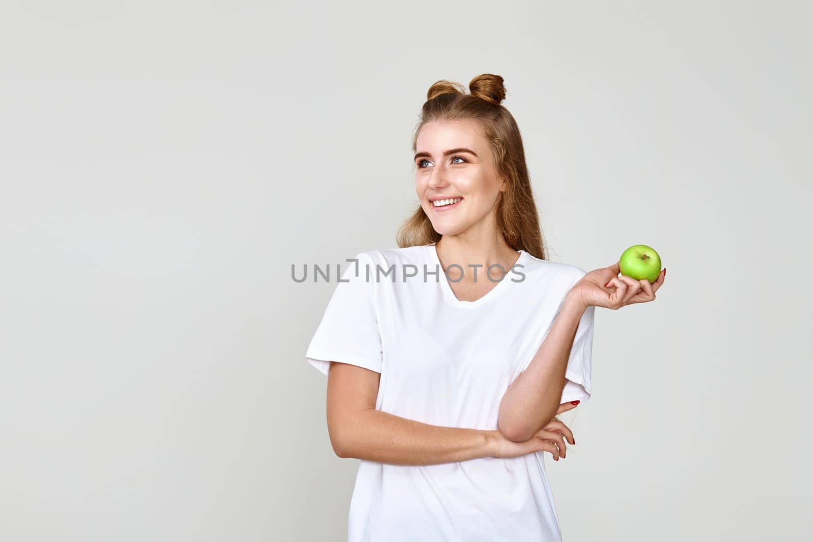 smiling pretty girl holding green apple and looking at copy space isolated on studio background.