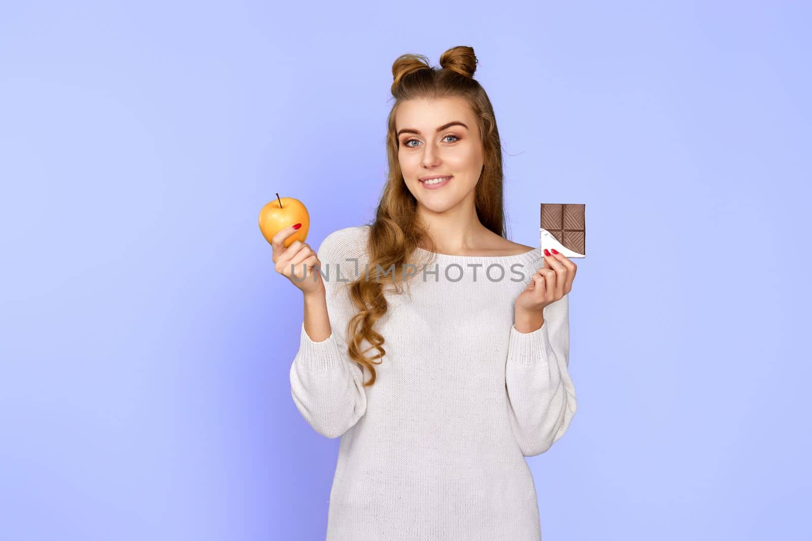 young happy woman making choice between healthy apple and unhealthy chocolate isolated on pastel violet background. Delicious and harmful