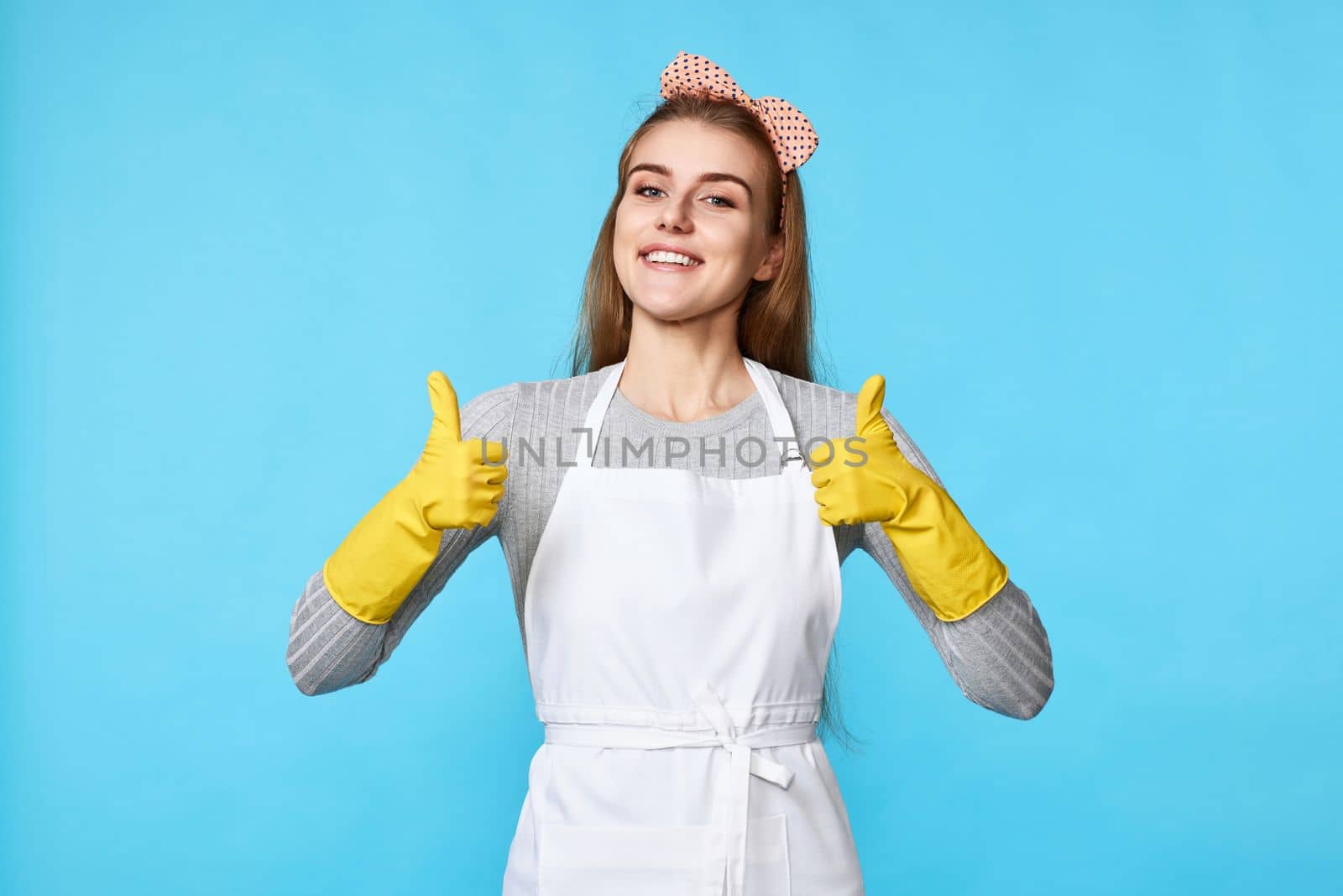 beautiful happy woman in yellow rubber gloves and cleaner apron showing ok sign isolated on blue background. cleaning