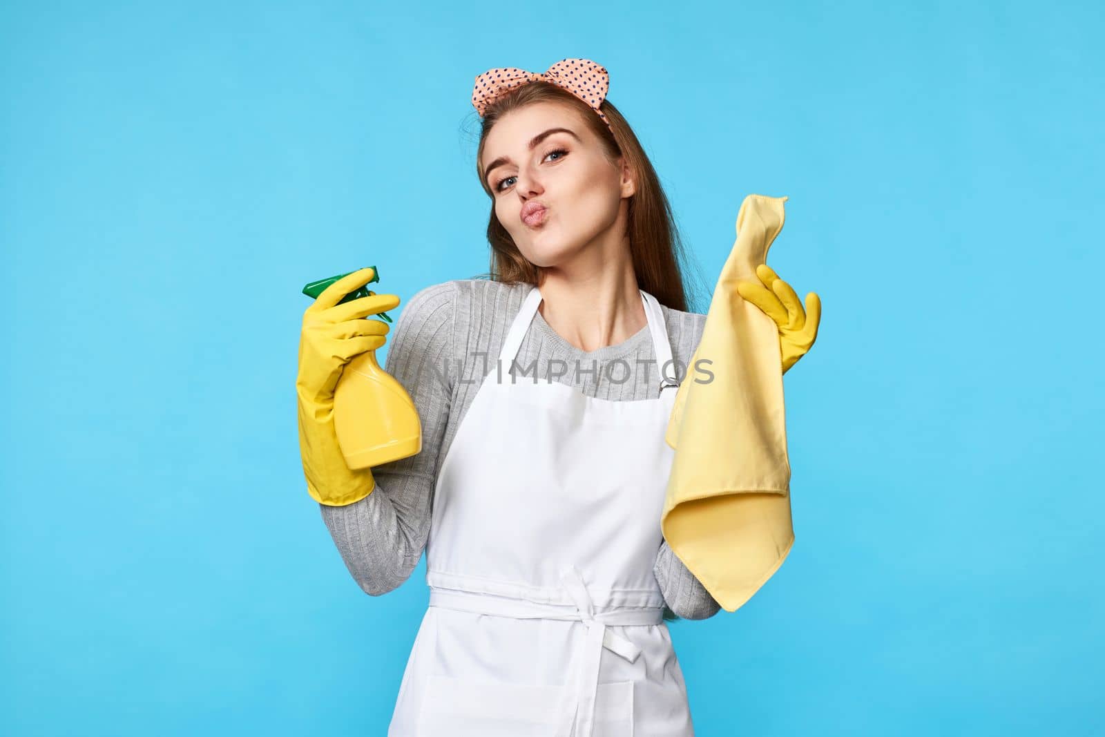caucasian woman in yellow rubber gloves and cleaner apron with cleaning rag and detergent sprayer isolated on blue background. cleaning