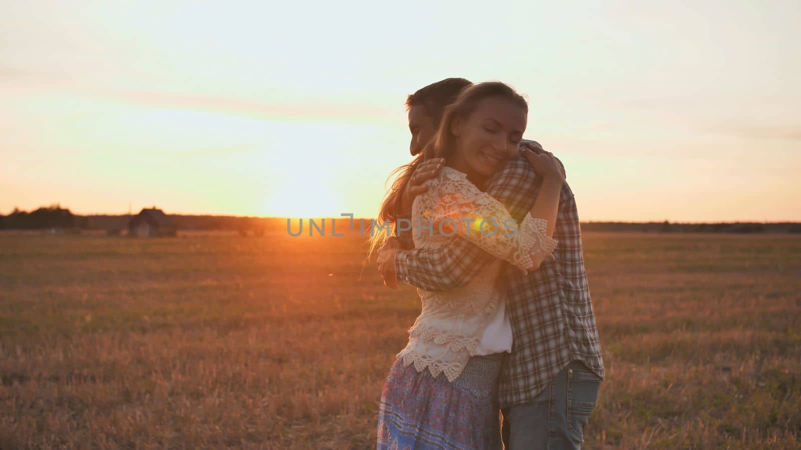 A guy is circling his girlfriend in his arms on a sunset background. by DovidPro