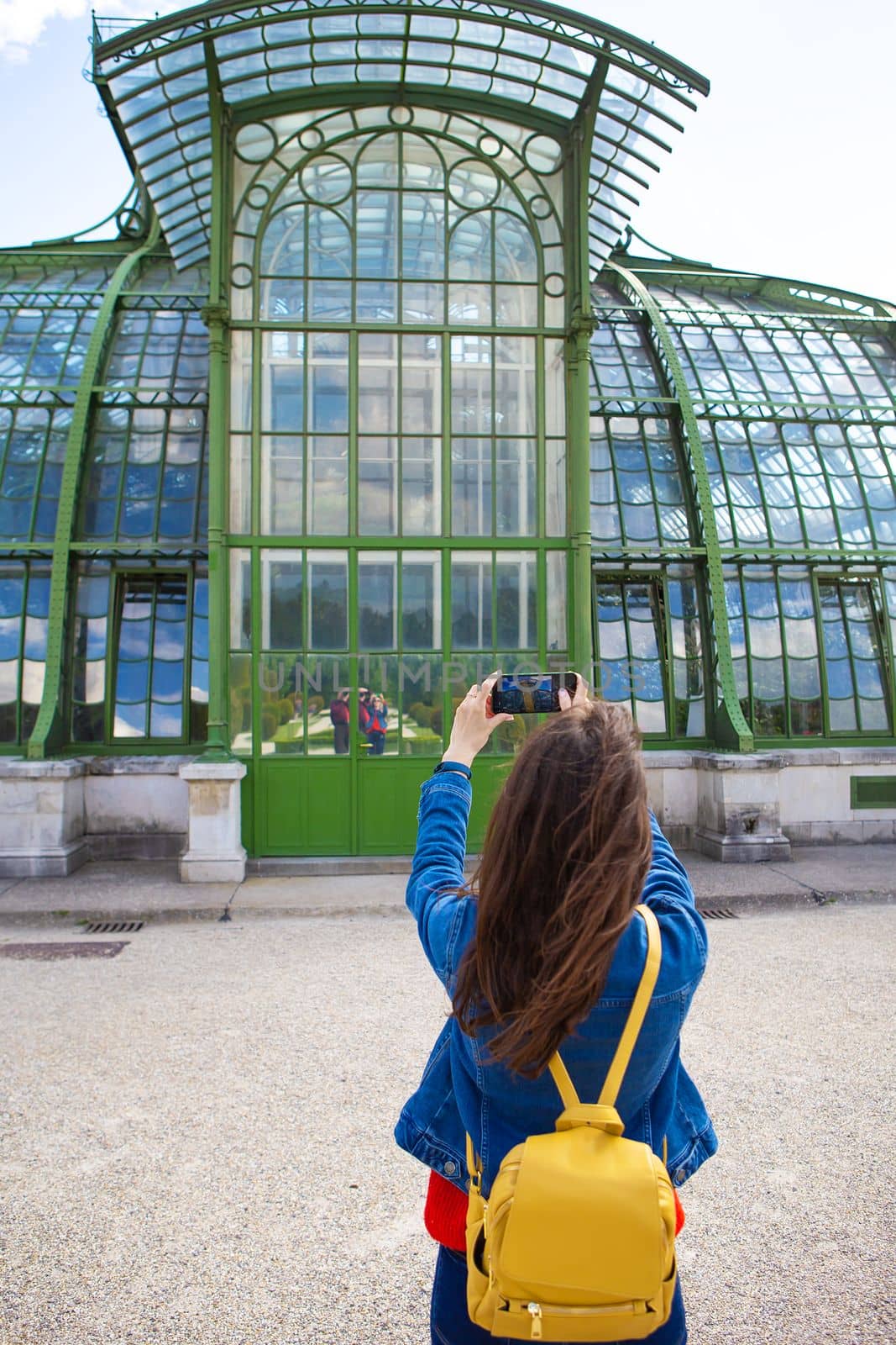 A young girl holds a phone in her hands and takes a picture of a beautiful building in Schonbrunn Park, Vienna