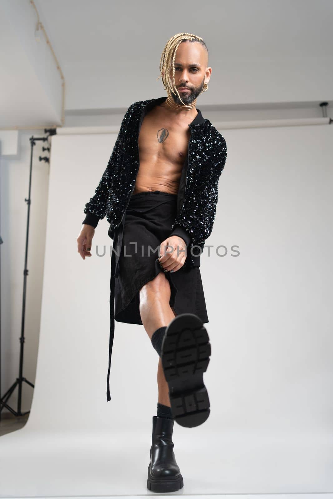 Full length gay man wearing women clothing dancing. Brazilian homosexual male wearing black skirt and boots posing in photo studio on white background. Bearded gay with make up. Vertical shoot