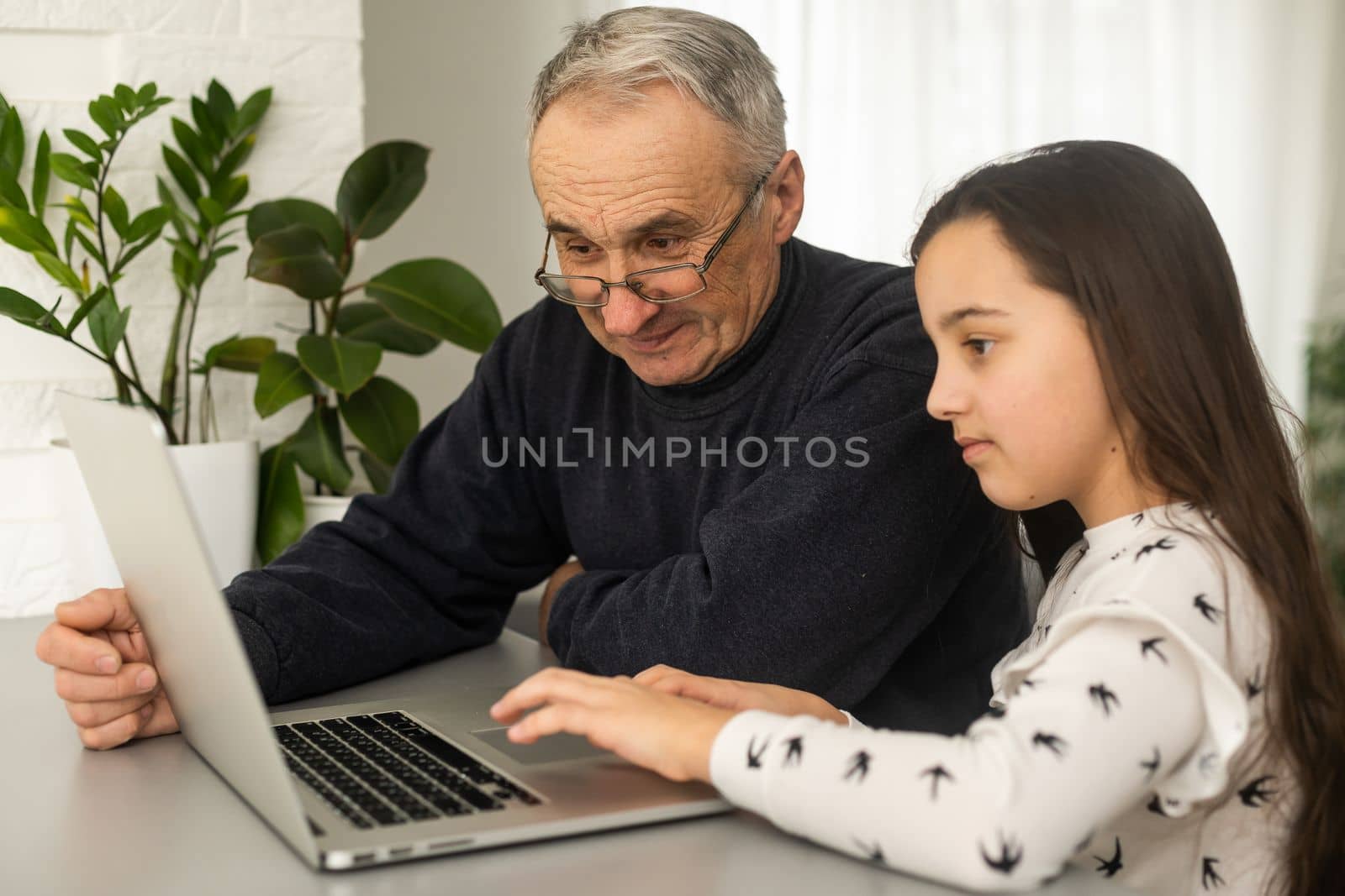 Portrait of grandfather and granddaughter doing homework with laptop. by Andelov13