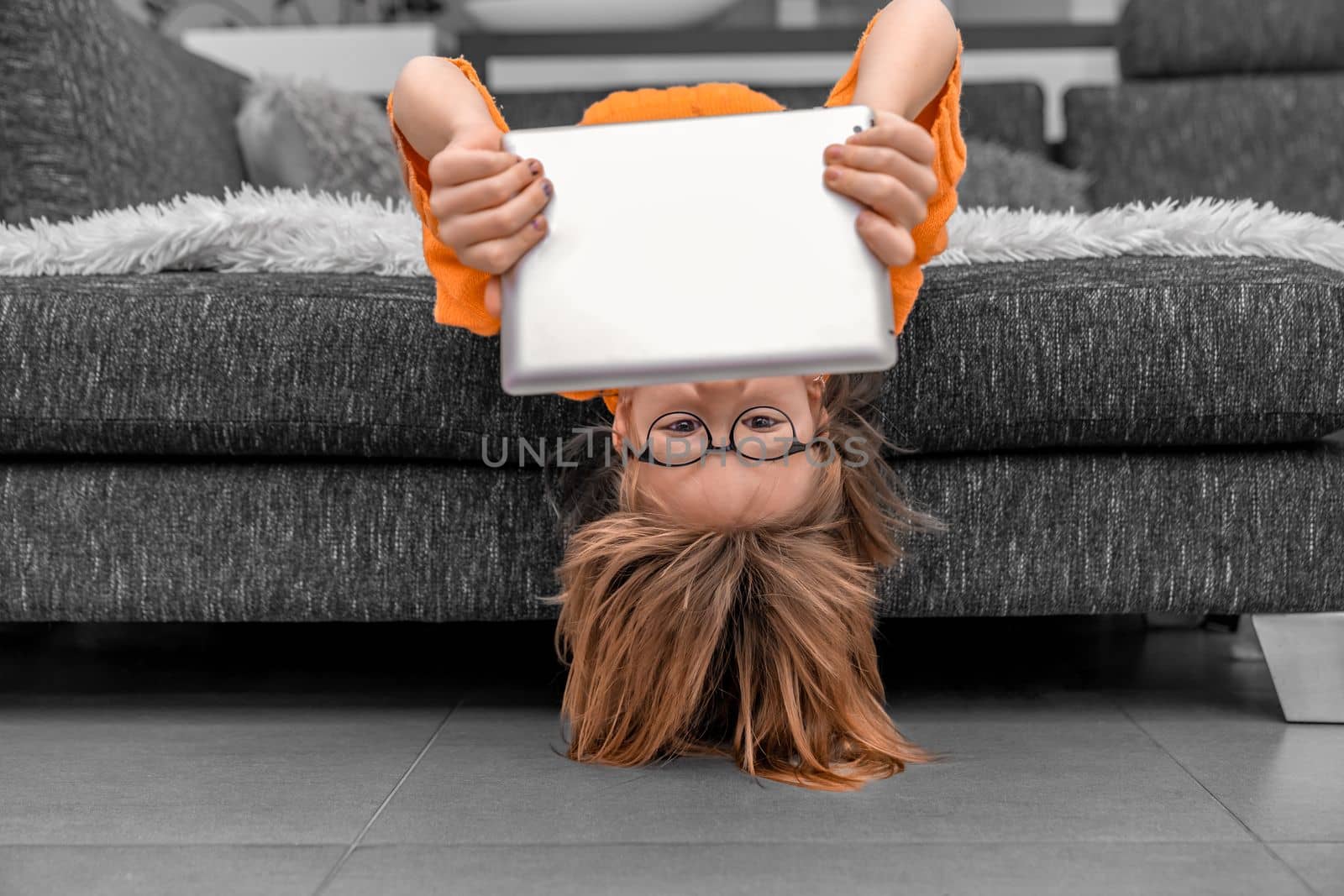 child with head down on sofa at home using tablet for online entertainment by Edophoto