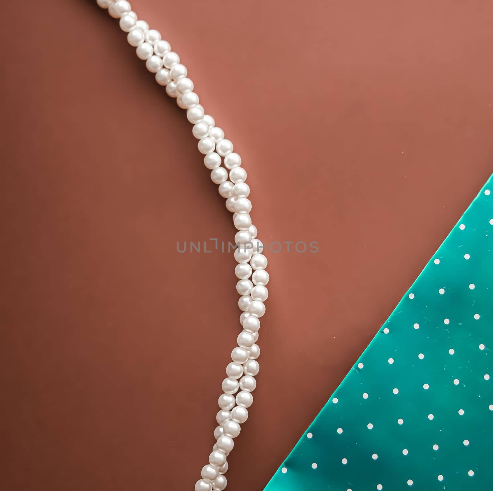 Pearl jewellery necklace and abstract green polka dot background on brown backdrop.