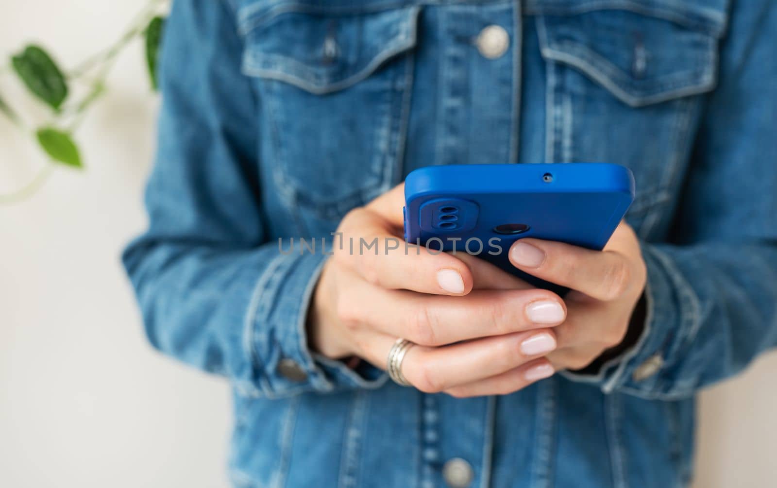 A girl in a denim shirt holds a smartphone in her hands. The concept of working online, freelancing, correspondence, chat. Close-up