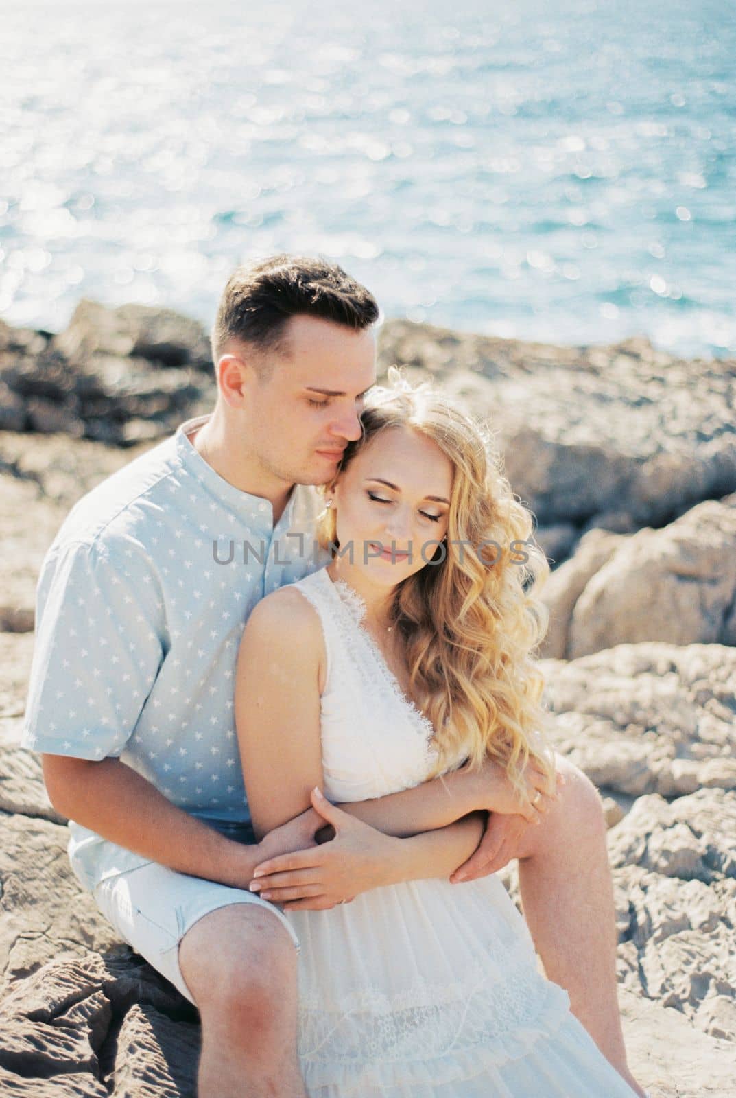 Man hugging a woman sitting on the rocks by the sea. High quality photo