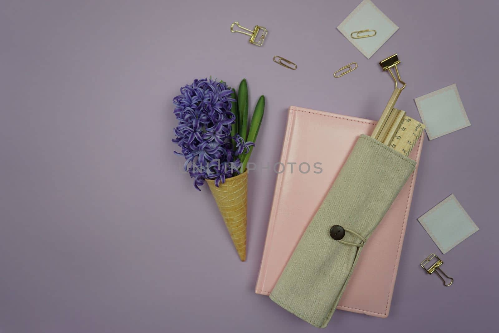 On the table is a pink notebook, stationery and a hyacinth flower in a waffle cone. Office of business lady Flatley. A freelancer's workplace on a public holiday.