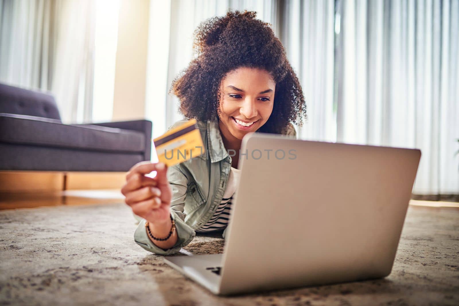 Shopping from home, who would have thought. a cheerful young woman doing online shopping on her laptop while lying on the floor at home. by YuriArcurs