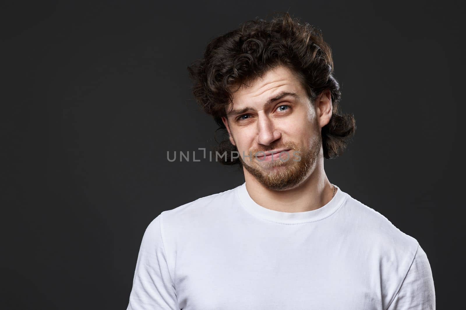 skeptic and frowning man in white t-shirt looking suspicious on dark gray background