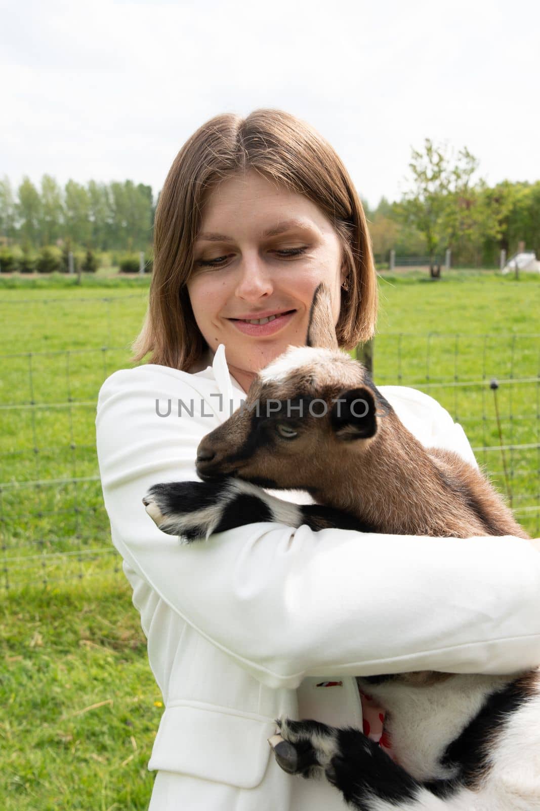 Young woman plays with goat kids, feeding them, sun shining over farm in background, High quality photo