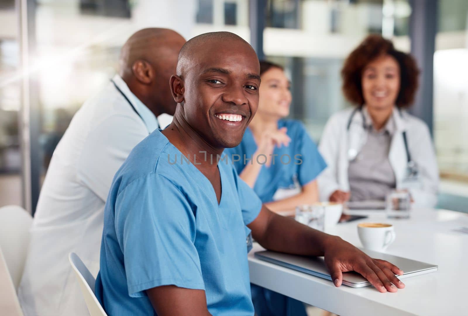 He is happy to be saving lives. Portrait of a cheerful young doctor seated at a table during a meeting inside of a hospital during the day