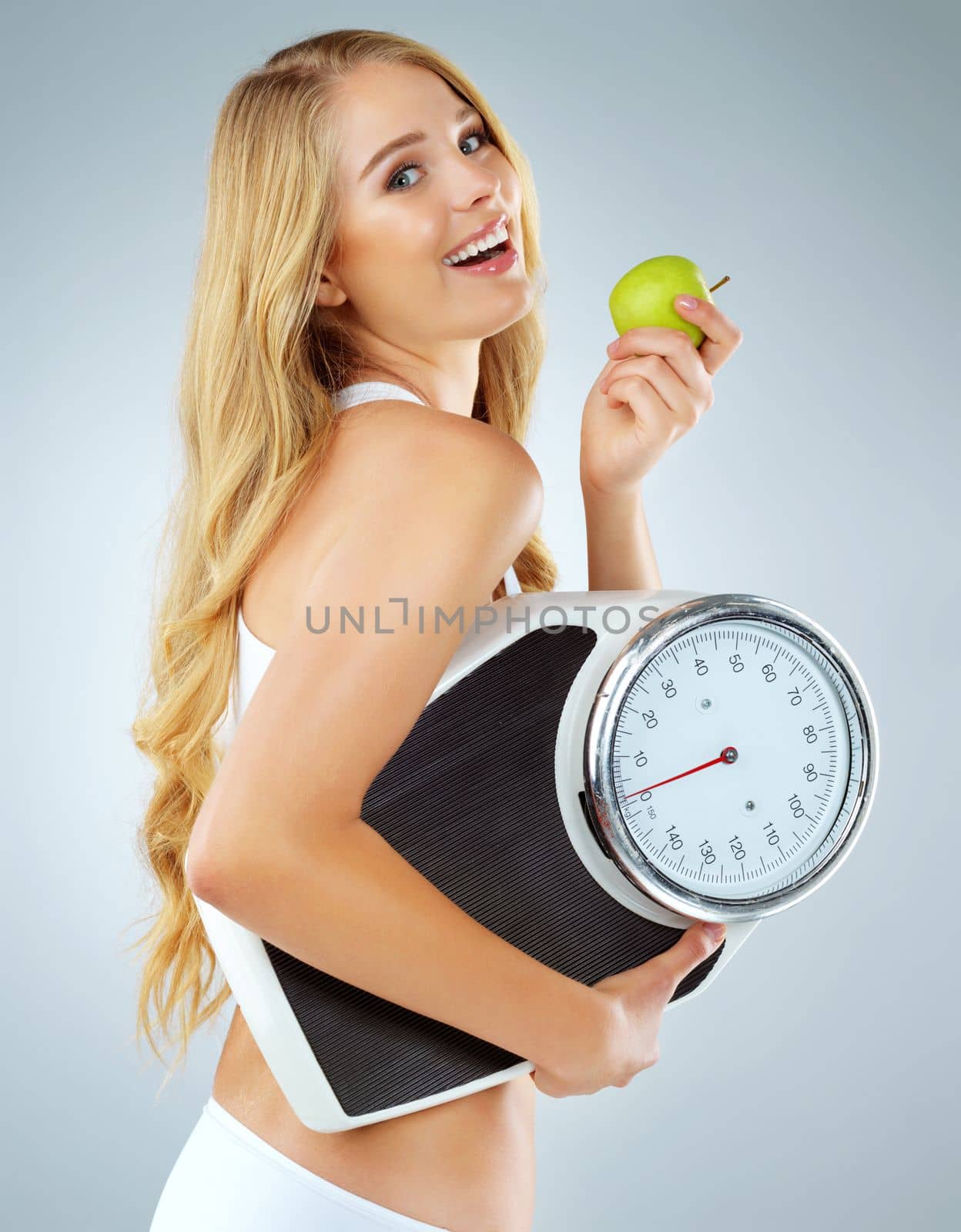 Ive found a combination that works. Portrait of a health-conscious young woman posing with an apple and a scale in studio. by YuriArcurs