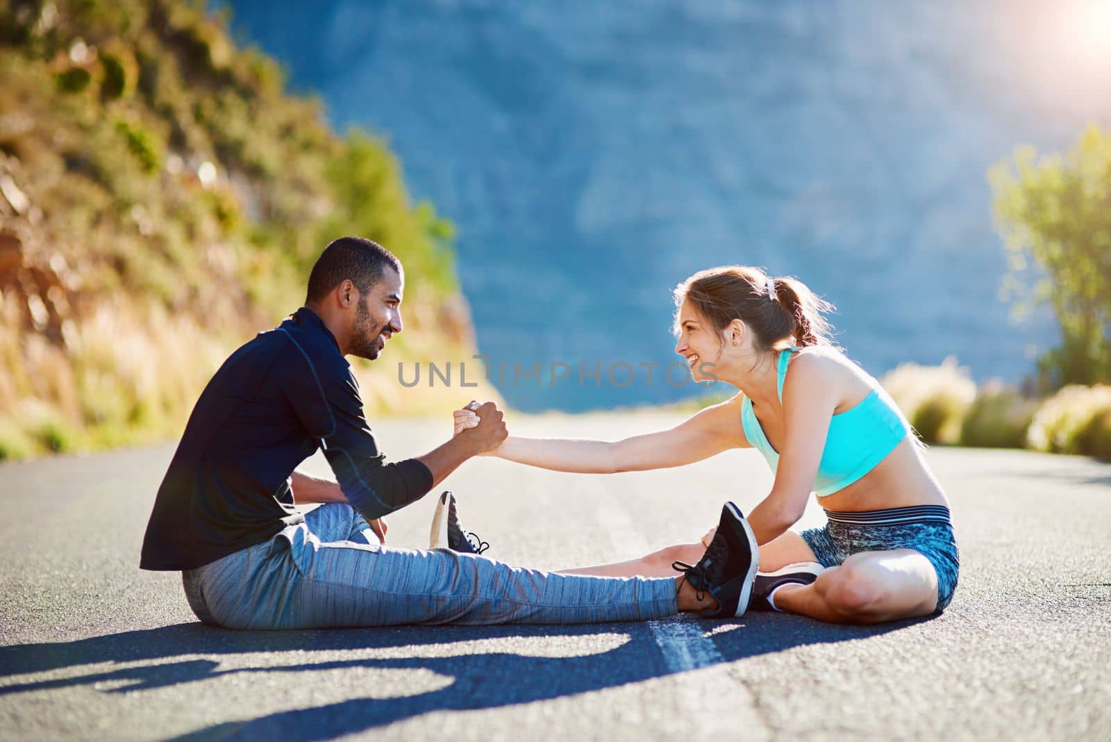 Stretching it out with some help. a sporty young couple stretching before a run outside. by YuriArcurs
