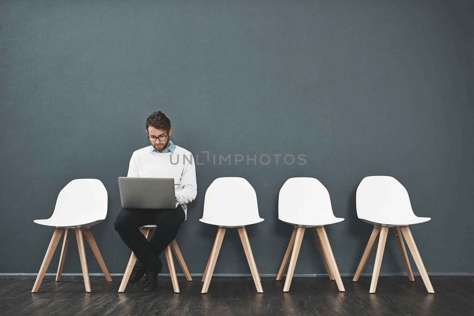 Keeping himself occupied while he waits. a young man using a laptop while waiting in line for a job interview