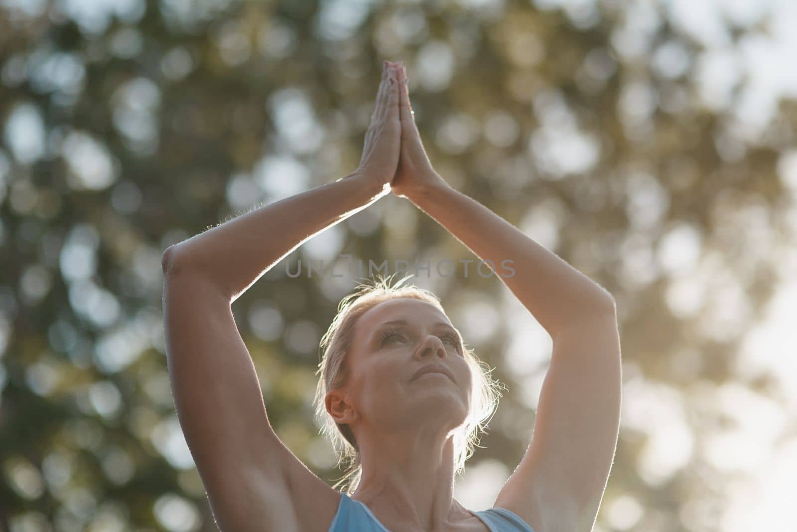 Nature brings peace to all. mature and fit woman engaging in a standing yoga pose with her hands touching above her head