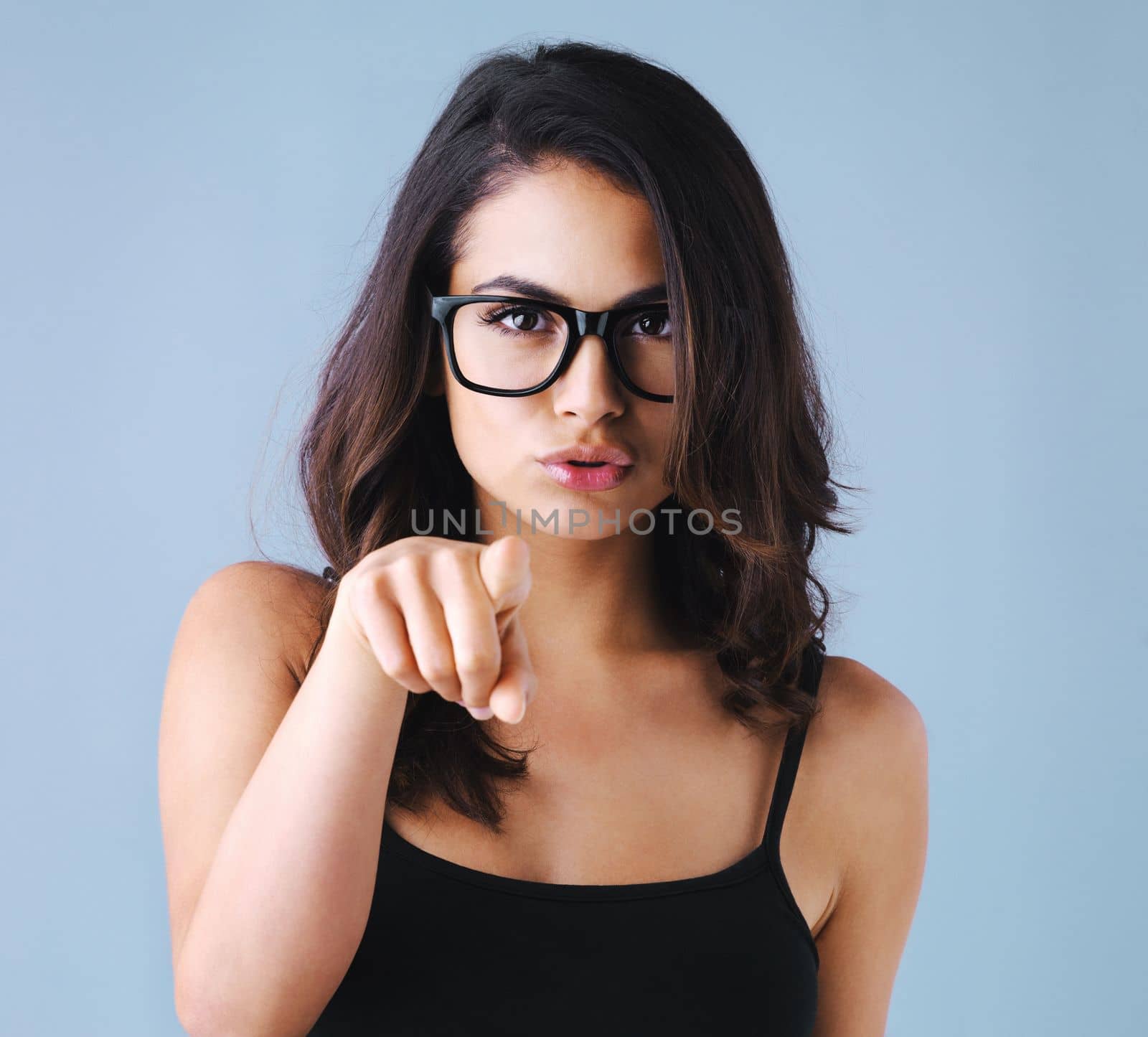 Is this your doing. Studio shot of an attractive young woman pointing and looking unhappy against a gray background