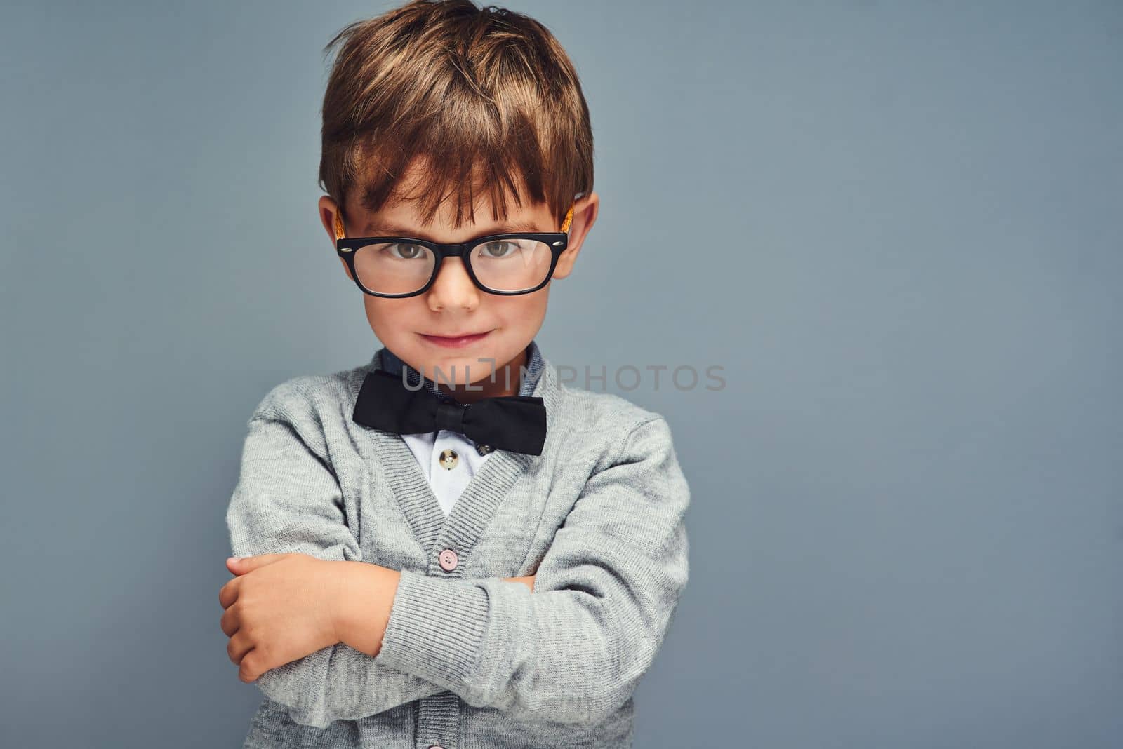 Its cool to be clever. Studio portrait of a smartly dressed little boy posing confidently against a gray background. by YuriArcurs