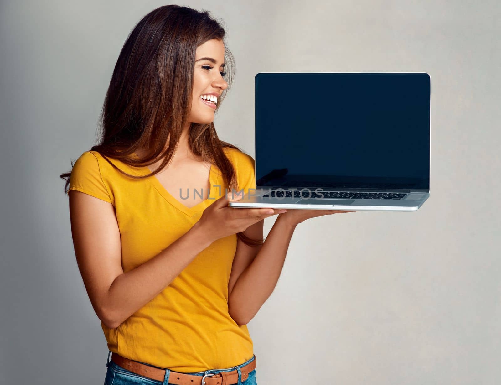 Be a part of something bigger online. Studio shot of an attractive young woman holding to a laptop with a blank screen against a grey background. by YuriArcurs