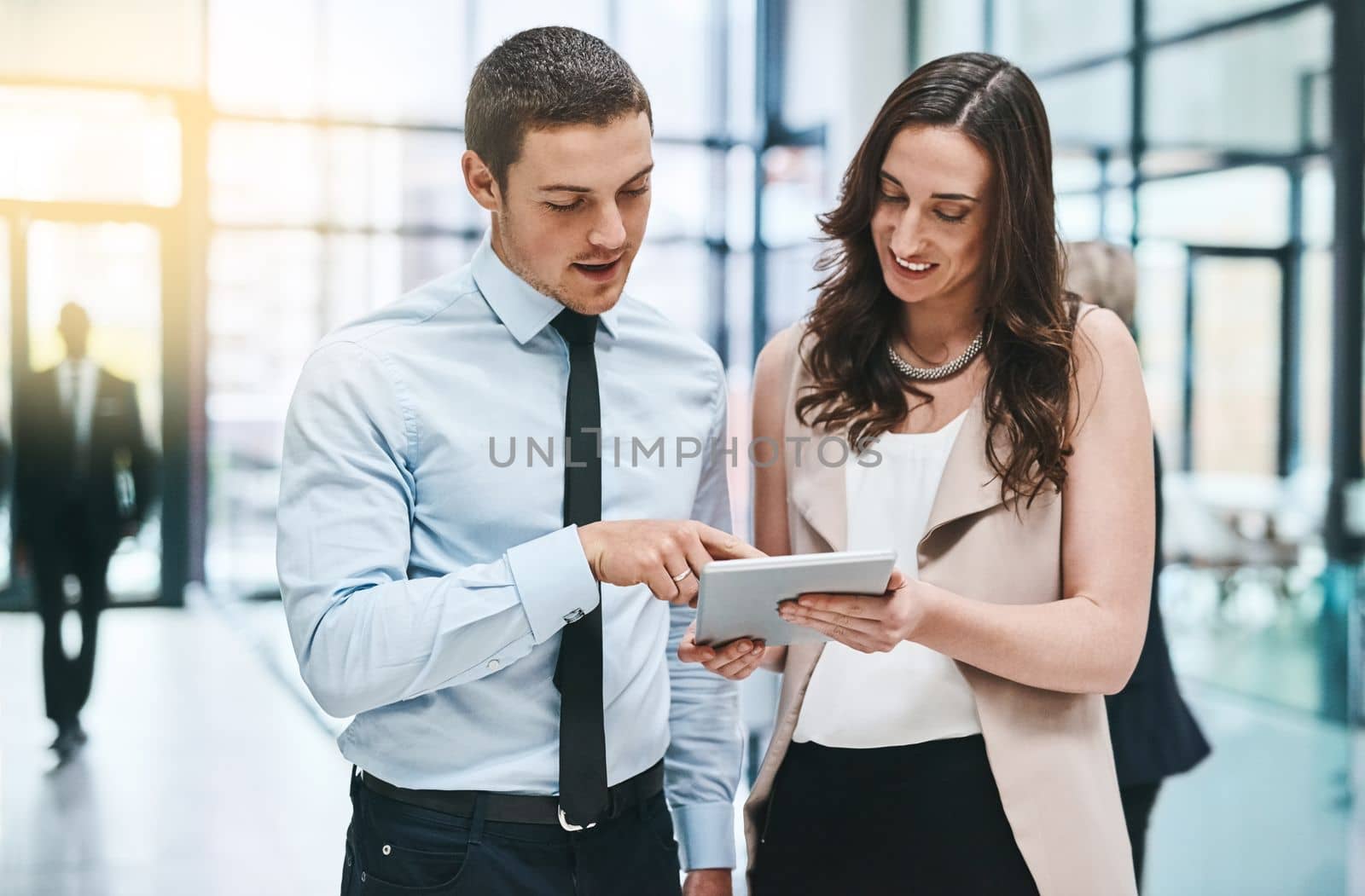 Everything is easier together. two young businesspeople working on a digital tablet in a busy office